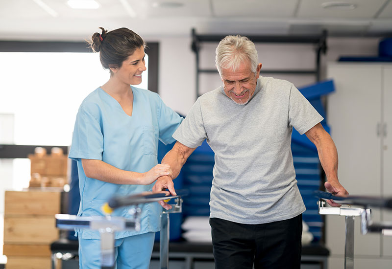 Senior man uses parallel bars to walk during physical therapy in Shreveport