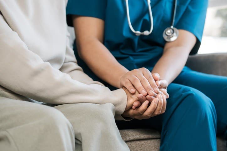A nurse comforts an elderly woman by holding her hand