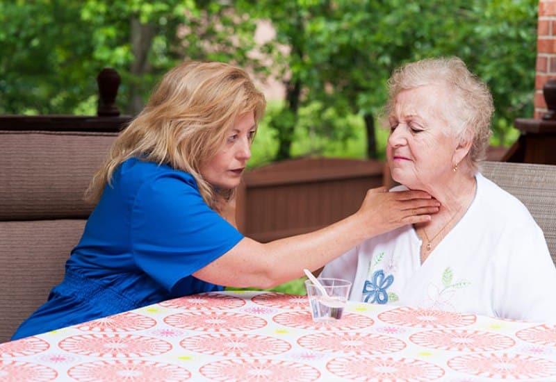A woman therapist assists an older woman with her neck during speech therapy at a nursing and rehabilitation center