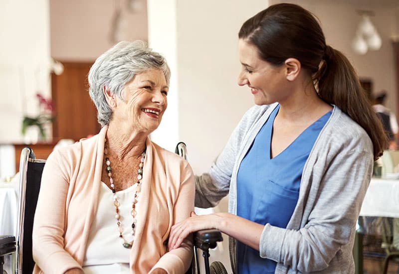 Elderly woman and nurse talk in a skilled nursing facility dining room