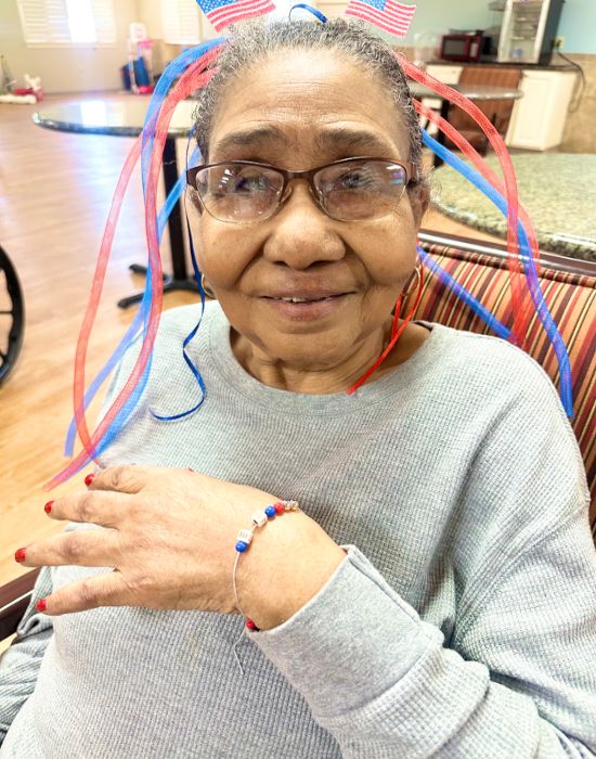 An older woman with red, white, and blue ribbons in her hair accessories smiles at the Nursing and Rehabilitation center