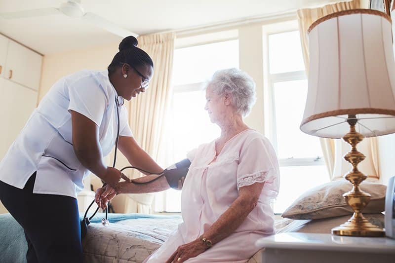 A nurse checking the blood pressure of a an elderly woman patient in a skilled nursing facility