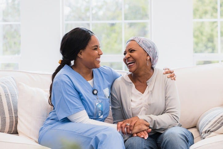 Two women in scrubs sitting on a couch, discussing hospice and palliative care